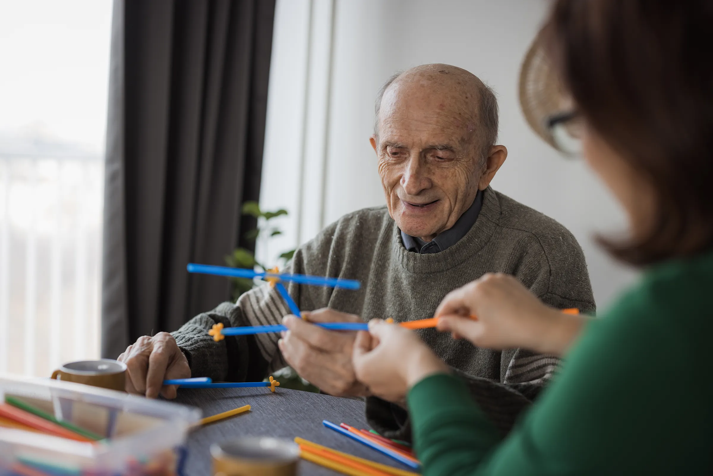 Elderly man assembling colorful construction sticks at table
