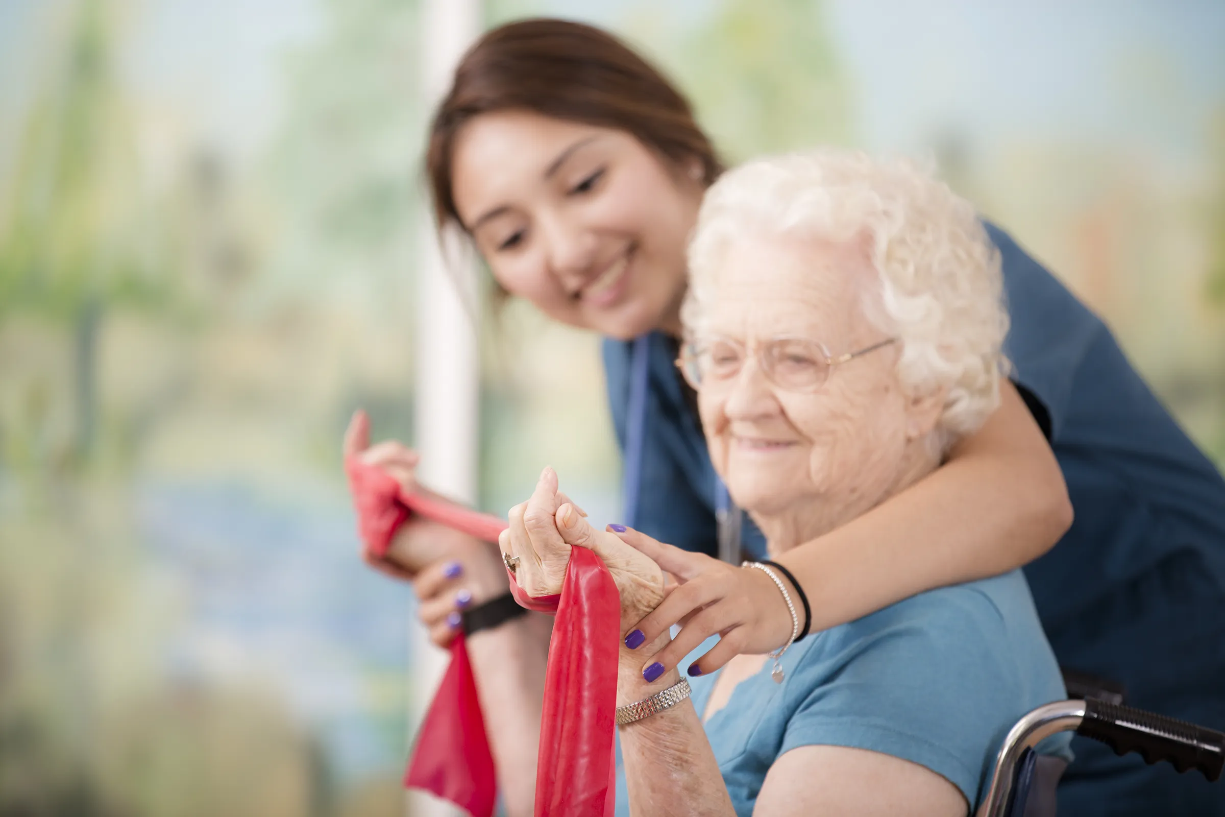 Caregiver assisting elderly woman with resistance band exercise